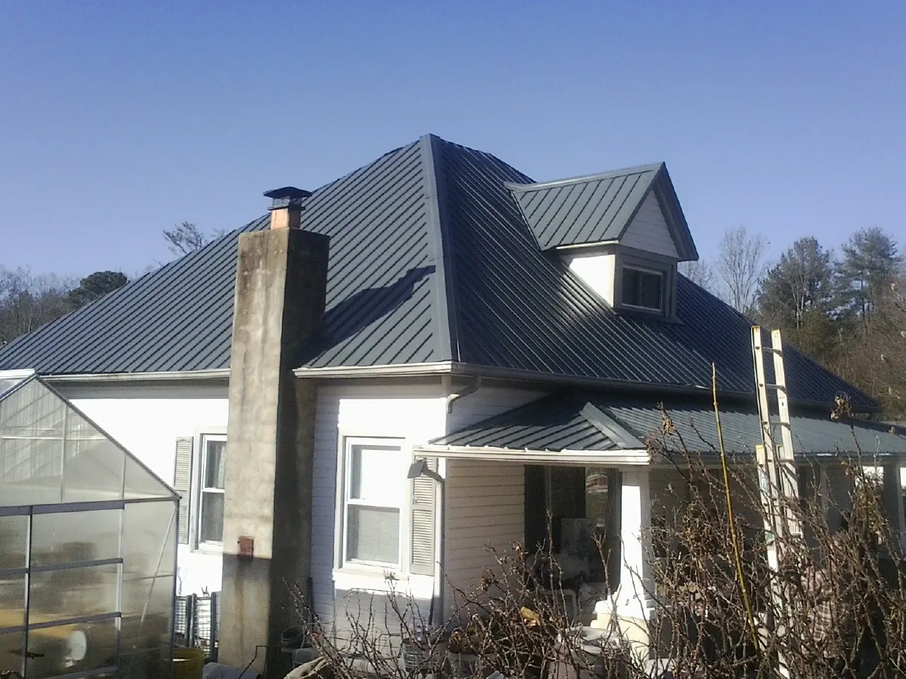 Dark blue standing seam metal roof on a white farmhouse with dormer — Slate & Tile Roof Repair by Roofing Brothers in Wingina
