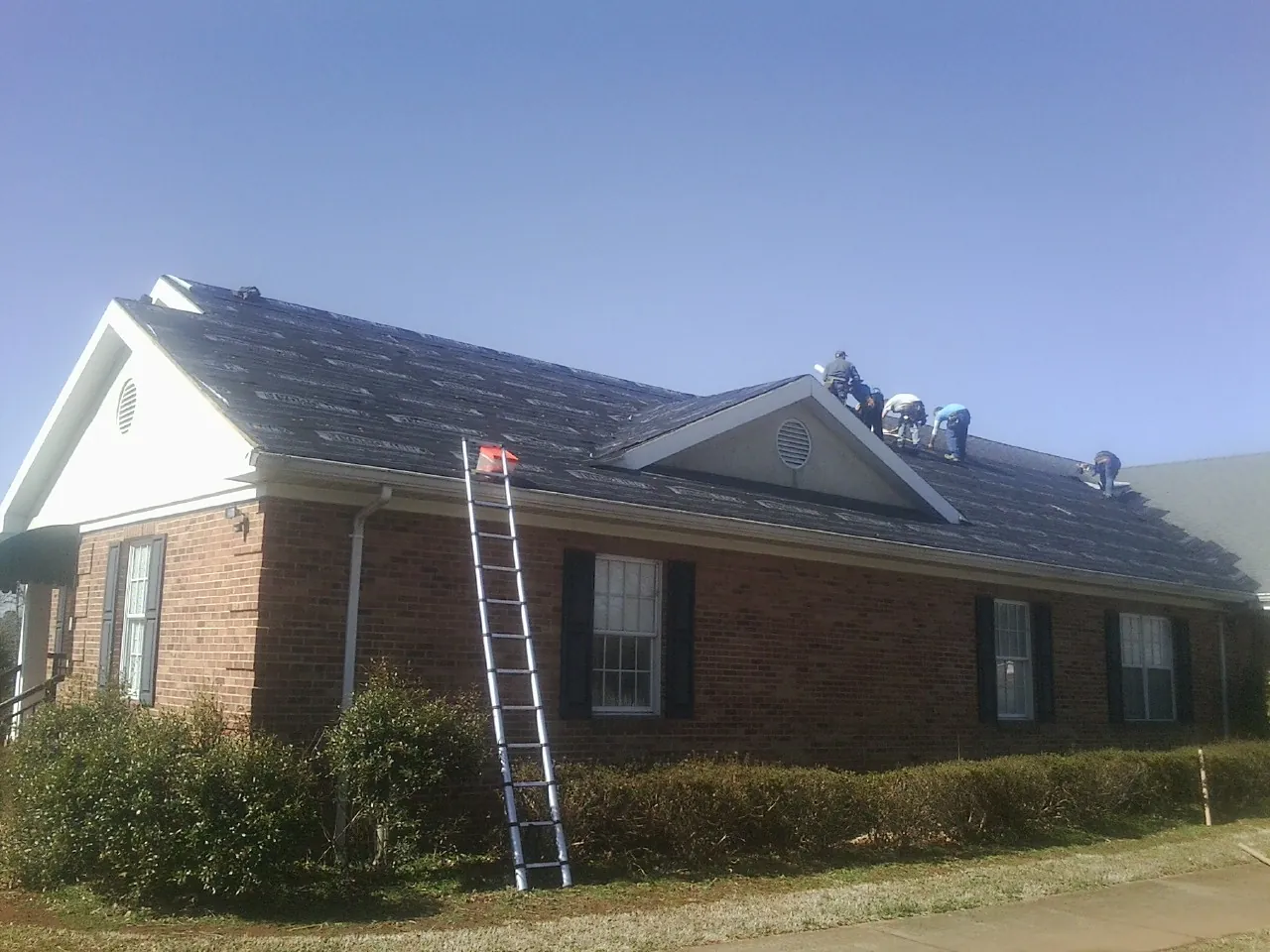 Crew tearing shingles off a brick ranch roof with a ladder set — Emergency Roof Repair work by our crew in Wingina