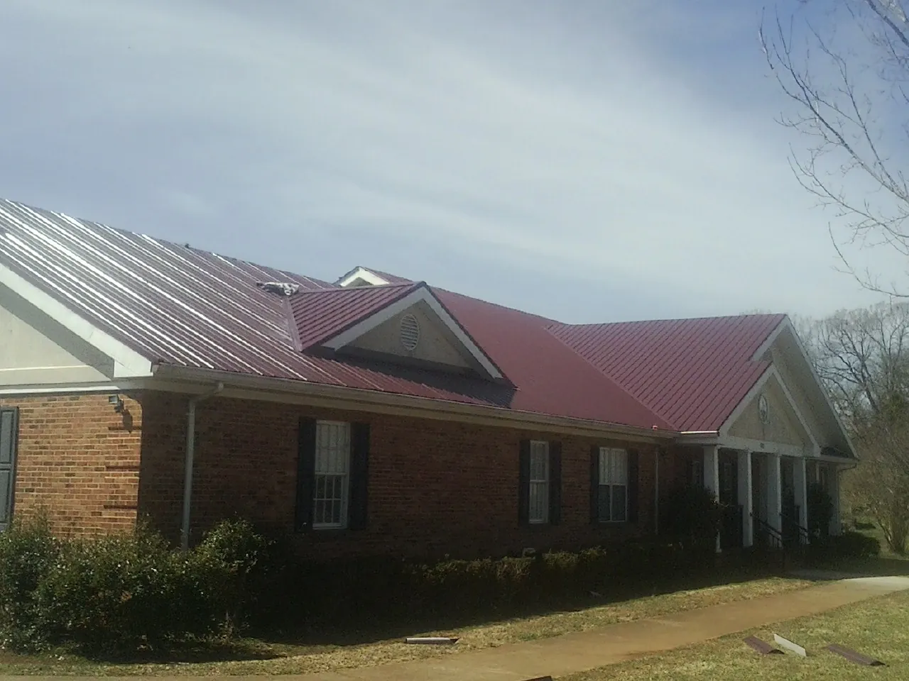 Red metal roof with gabled entries on a long brick building, from a Hail Damage Roof Repair job in Wingina