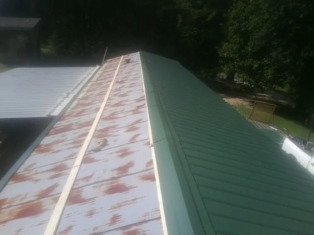 Old rusted panels beside newly installed green metal roofing — Wind Damage Roof Repair by Roofing Brothers in Wingina