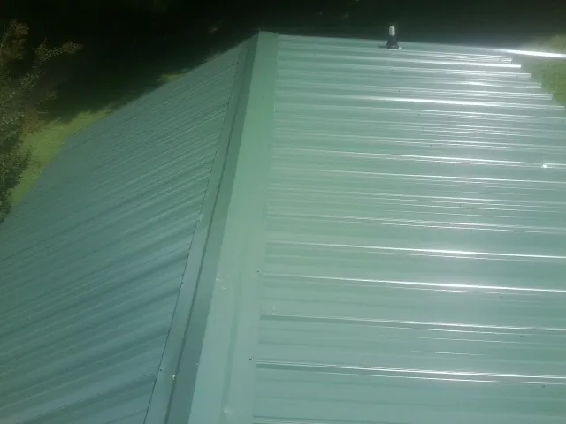 New green metal panels meeting at the ridge of a roof — Flat Roof Repair work by our crew in Wingina