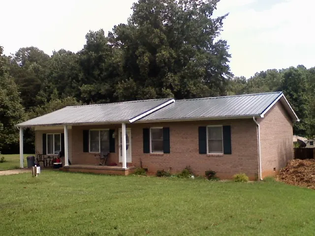 Gray metal roof on a brick ranch house with a side carport in Wingina