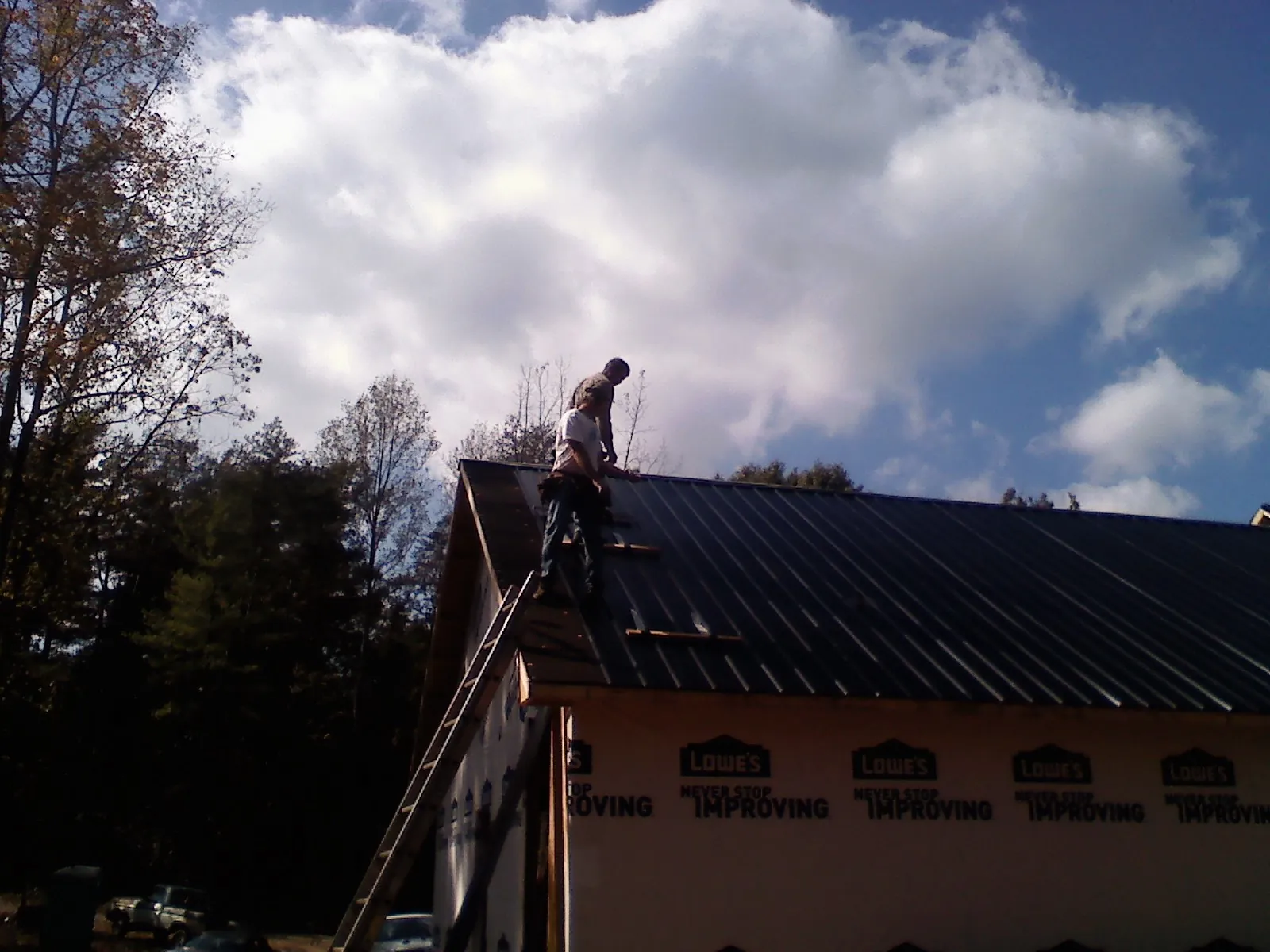 Roofer fastening dark metal panels high against a cloudy sky, from a Roof Inspection job in Wingina