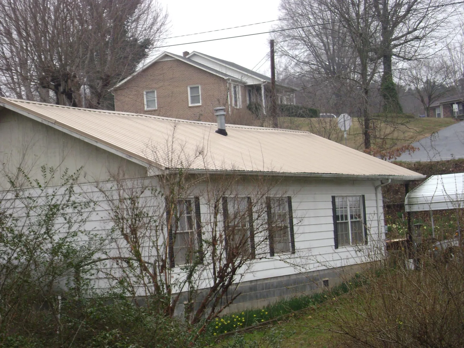 Tan metal roof on a white sided house set into a hillside — Commercial Roofing by Roofing Brothers in Wingina